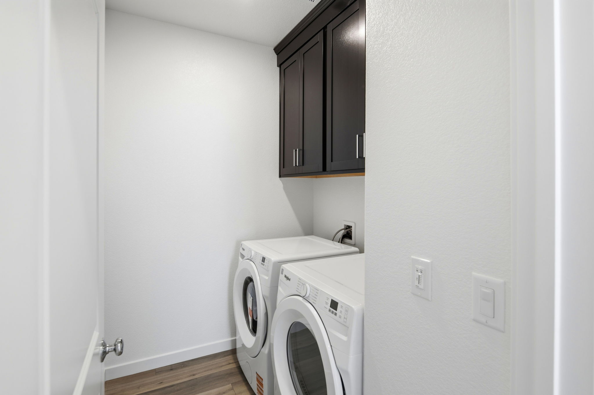 A white laundry room with a black cabinet and a white washing machine.