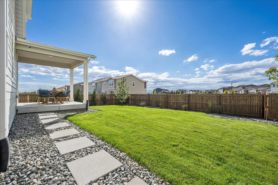 A backyard with a fence and a patio with a wood fence and a house and blue sky.