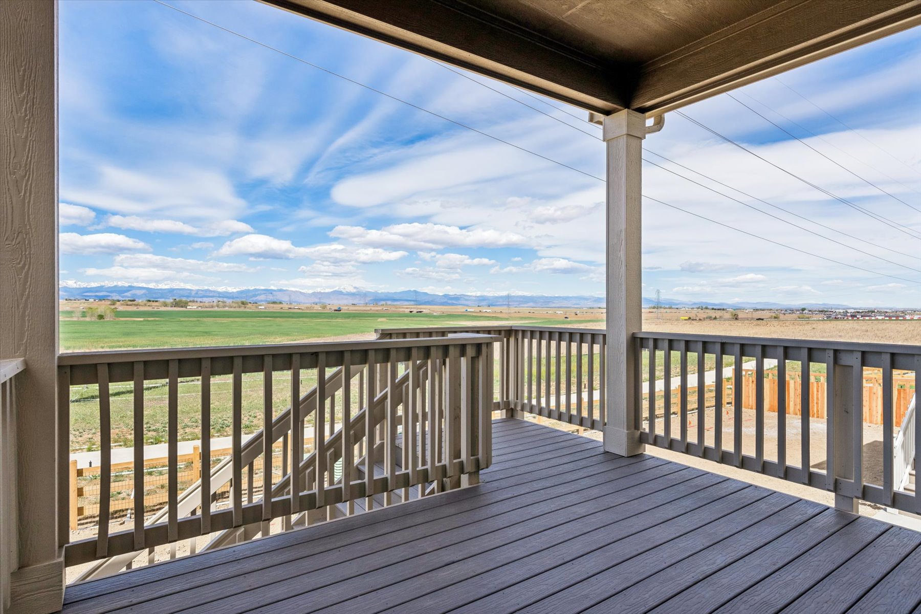 A wooden deck with a view of a field and blue sky.