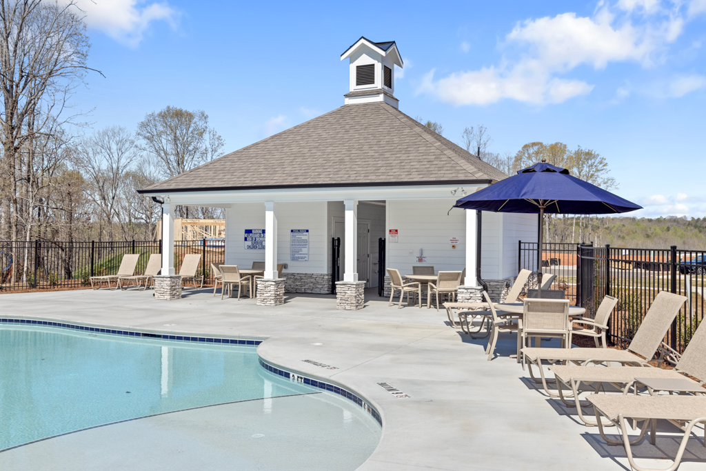 A pool with chairs and umbrellas by a house.